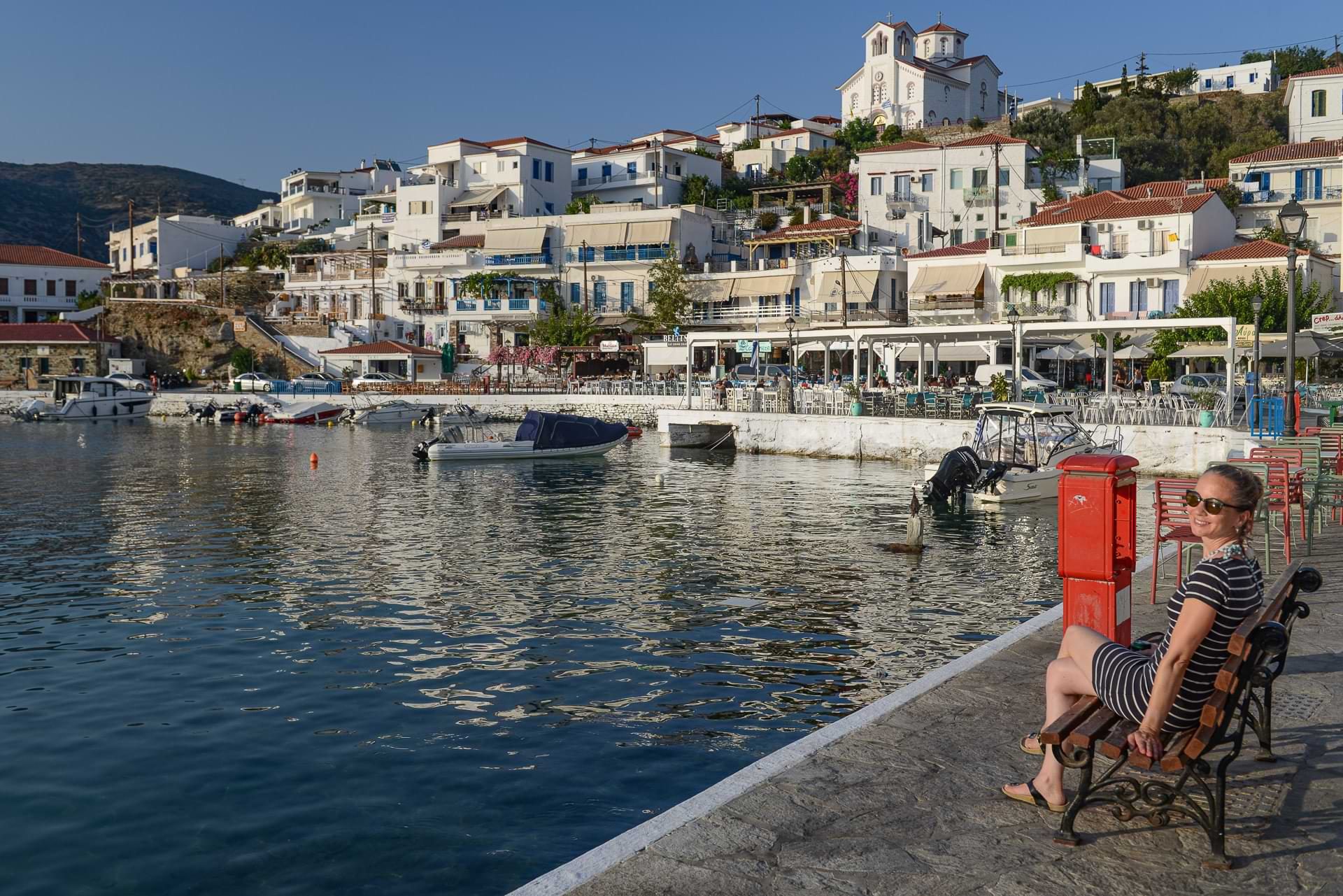 Im Küstenort Batsi auf der griechischen Insel Andros: Julia sitzt auf einer Bank am Meer und genießt den Blick auf die Häuser und den Hafen